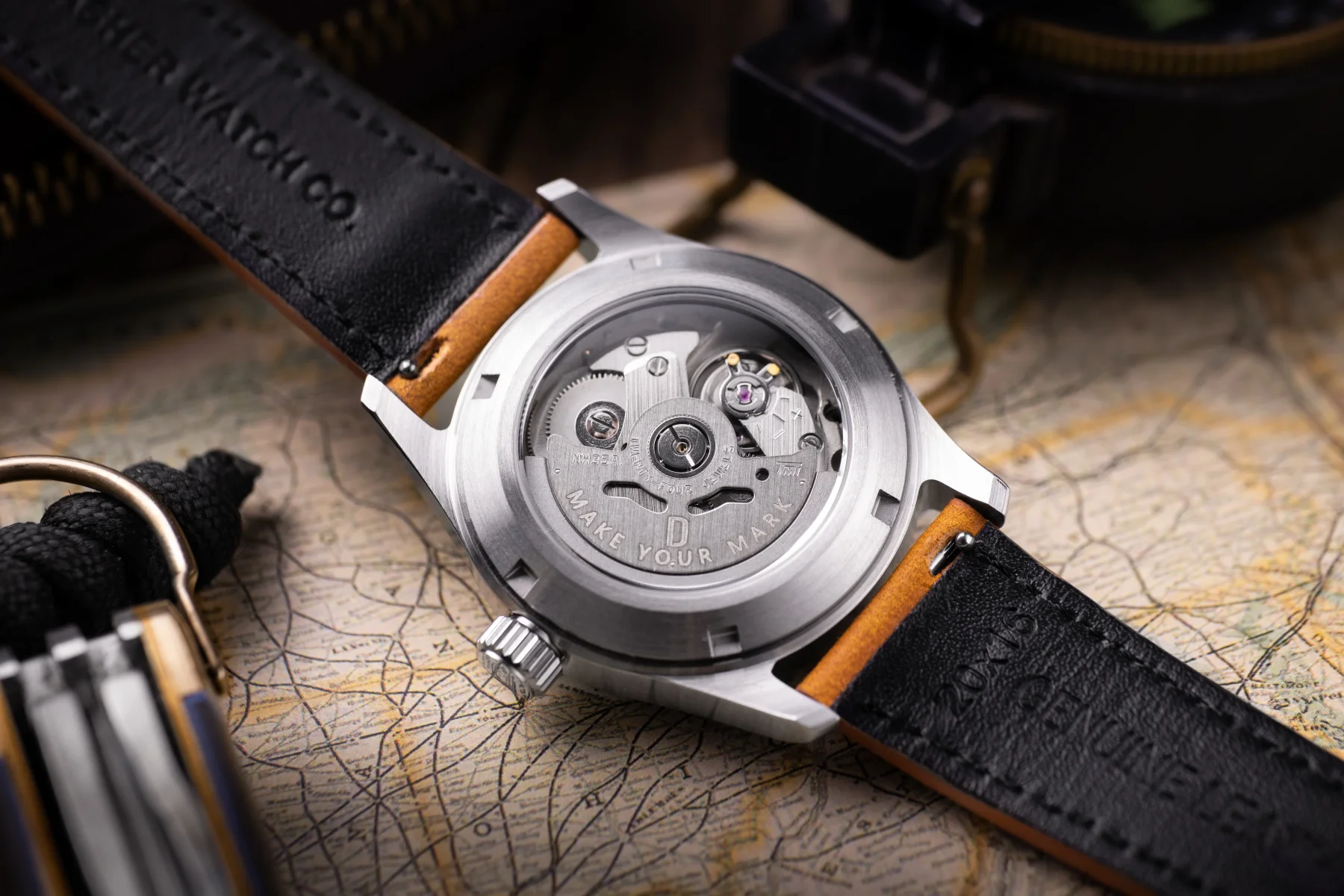 Dasher automatic watch back with exhibition caseback showing movement. Black & tan leather strap on map with compass.