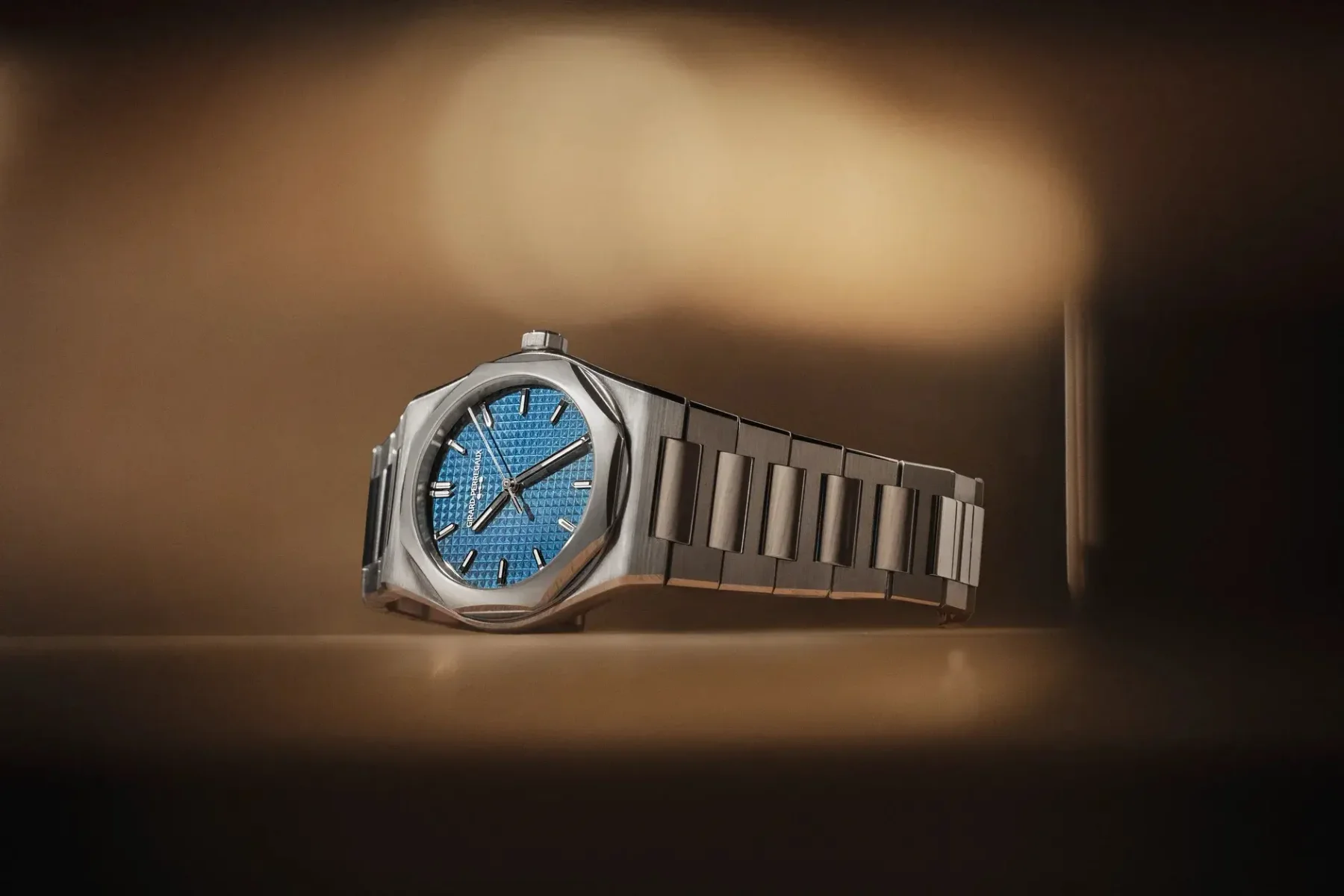 Steel Girard-Perregaux watch with a blue waffle-textured dial and integrated bracelet, showcased on a warm, dark background.
