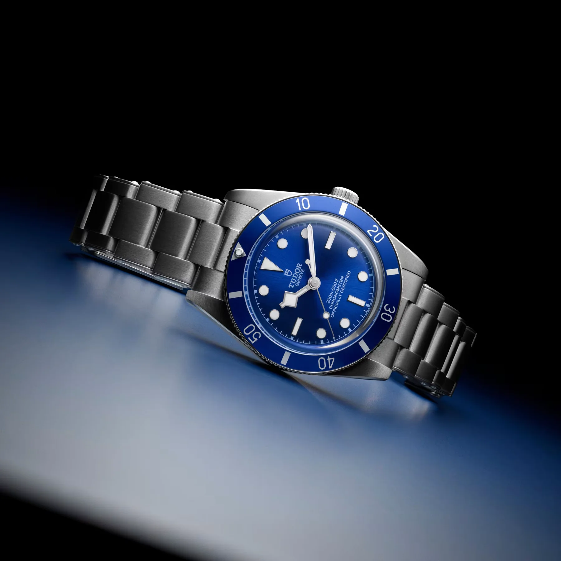 Tudor Black Bay 54 dive watch: blue dial, blue unidirectional bezel, brushed steel bracelet, angled on a blue gradient surface.