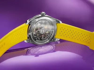 H. Moser & Cie. watch, back view, showing intricate mechanical movement and yellow perforated strap on purple surface.