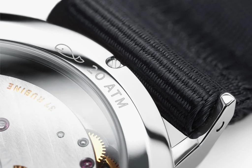 Nomos Ahoi watch case back: visible movement, '20 ATM' engraving with fish logo, and black woven strap.