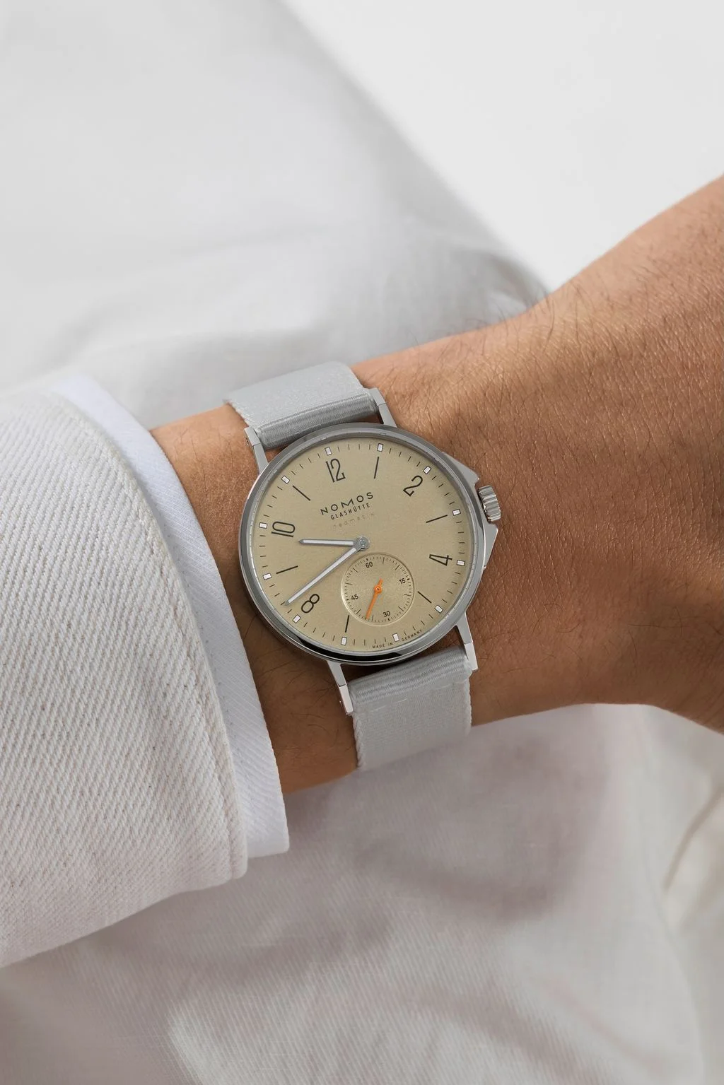 Close-up: Nomos Ahoi Neomatik 36 Sand dial watch on a wrist, with a light grey strap and white shirt cuff.