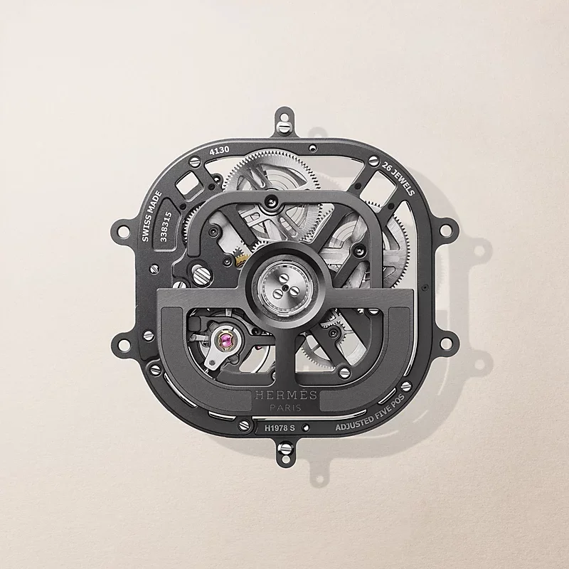 Skeletonized dark grey Hermes Swiss Made watch movement, showing gears, bridges, and a pink jewel.