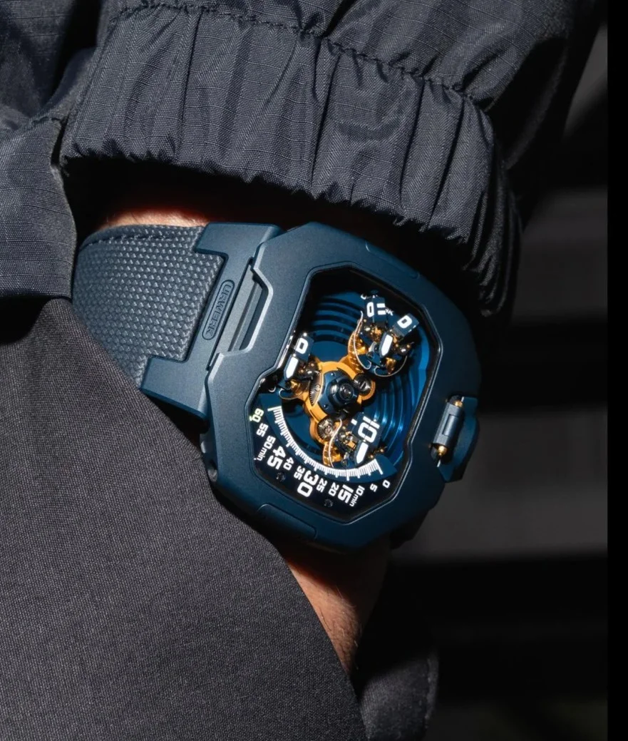 URWERK UR-120 "Spock" watch on wrist, dark blue case, visible gold mechanism, luminous white markers.