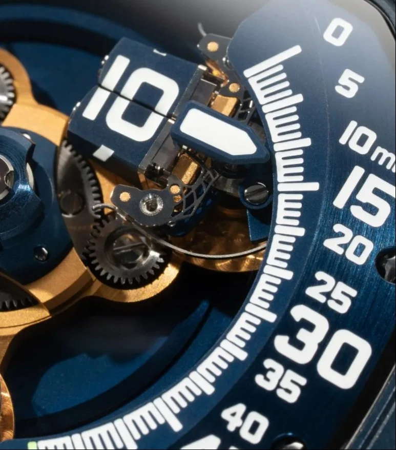 Macro of URWERK UR-120 watch, blue dial, exposed gold gears, white split "10" hour display & minute track.