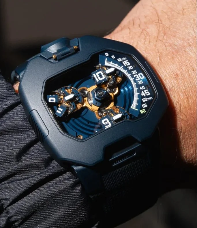 URWERK UR-120 "Spock" watch on a wrist. Dark angular case, exposed gold-toned gears, and blue satellite time display.
