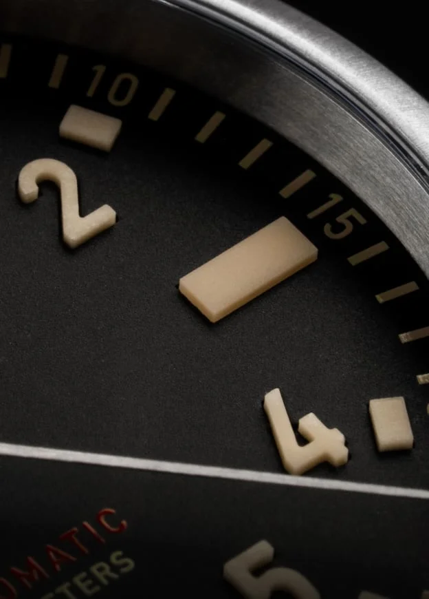 Close-up of Jack Mason Canton watch dial. Black dial, raised beige numbers '2', '4', bar marker, red "AUTOMATIC METERS".