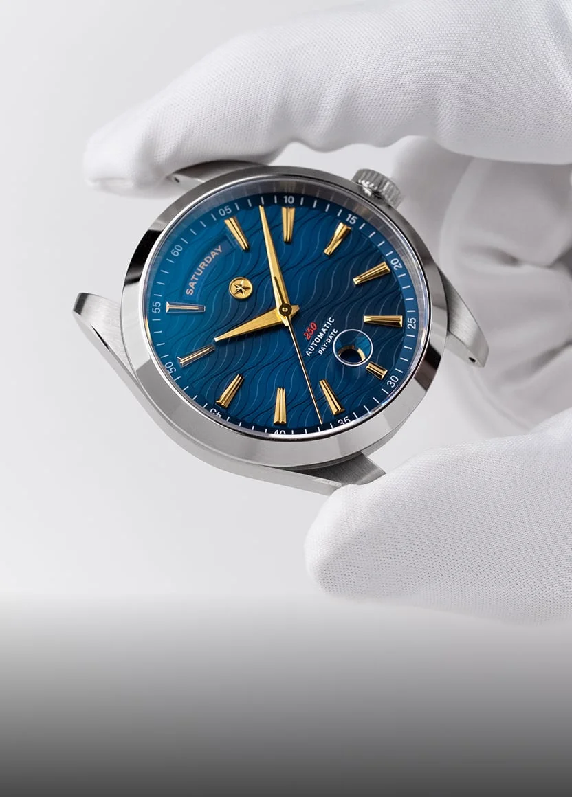 A hand wearing a white glove holds a silver wristwatch with a blue, wave-patterned dial and gold hands.