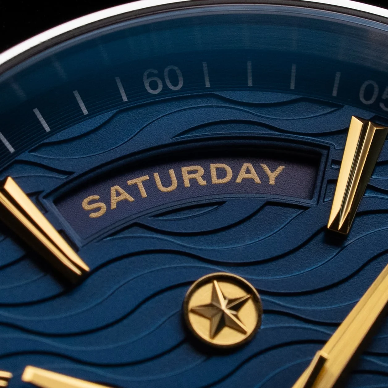 A close-up macro shot of a blue watch face with a wave pattern and gold hands and markers.