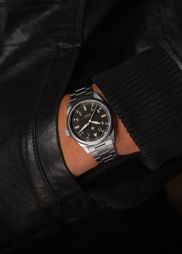Man's wrist wearing Jack Mason Canton Day-Date watch, silver case, metal bracelet, black dial with tan hour markers.