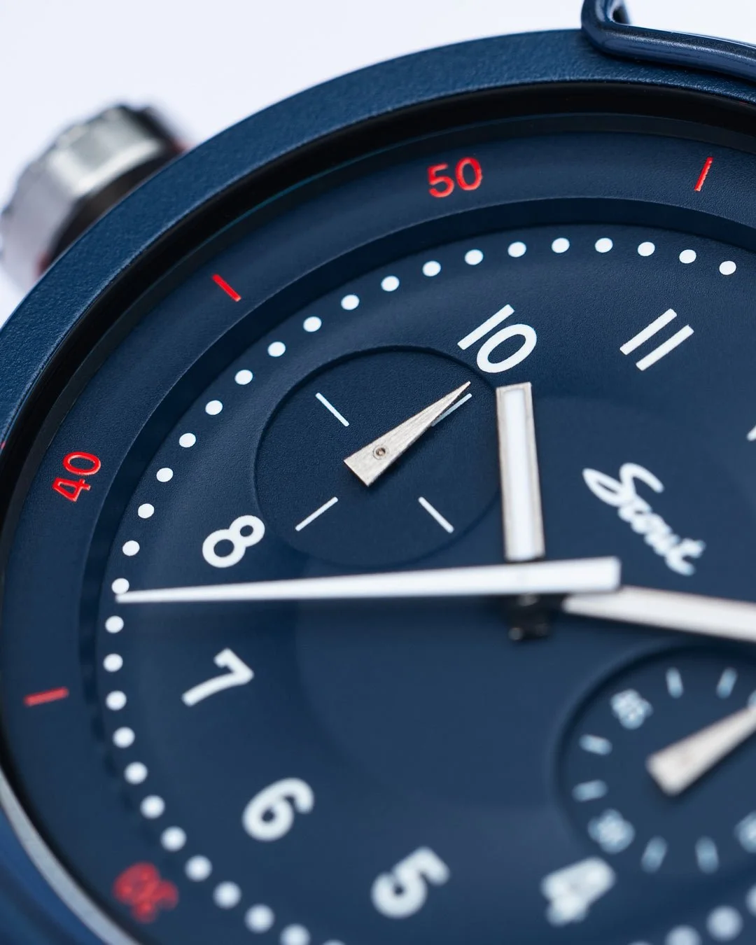 Close-up of VERO x Scout Workhorse Moonstone Blue watch dial with blue case. White numbers, red 40/50 markers, 'Scout' logo, silver hands.