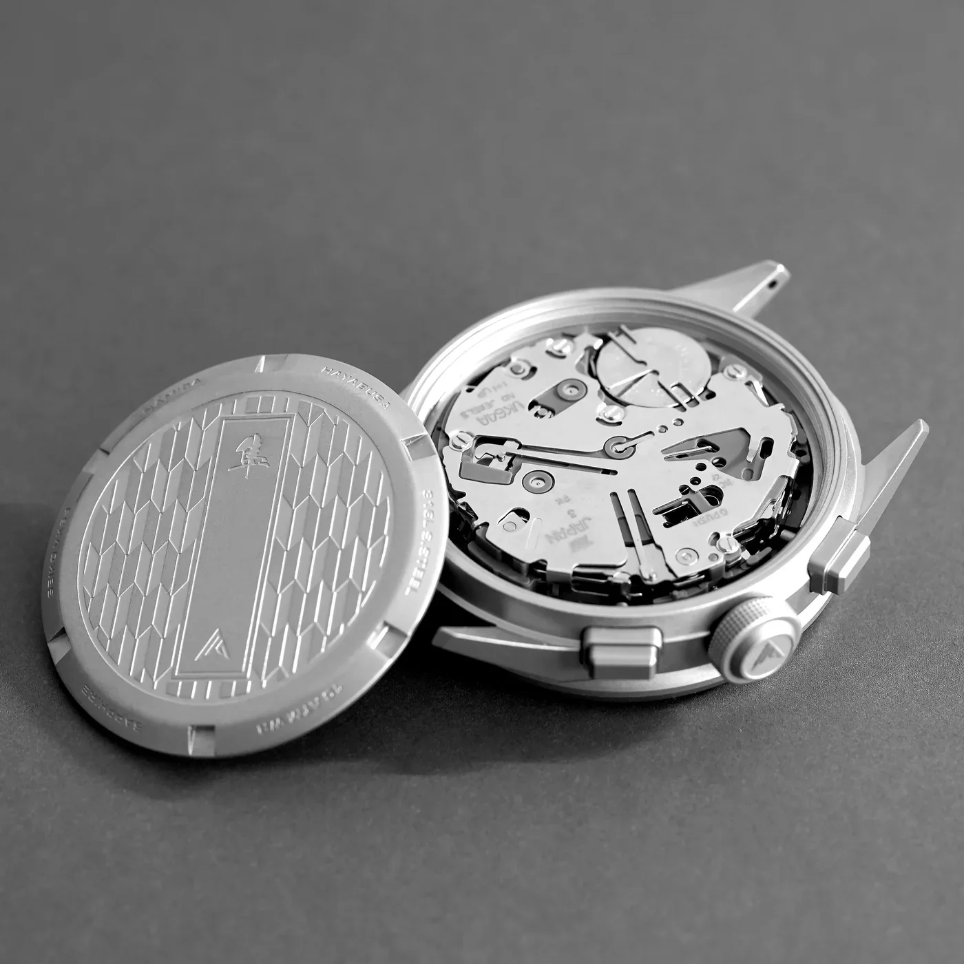Silver watch with open, engraved case back revealing a quartz movement and battery on a grey surface.