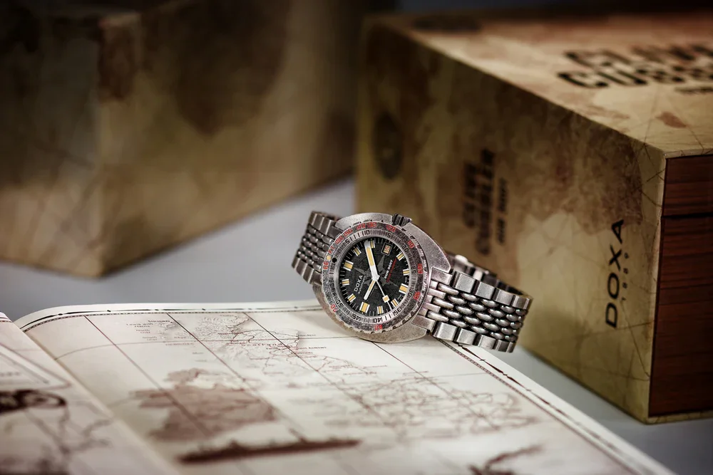Doxa SUB 300 dive watch with steel bracelet on an open vintage map, with blurred boxes in the background.