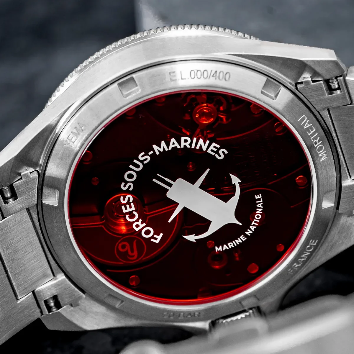Brushed steel watch caseback with red exhibition window revealing movement and 'FORCES SOUS-MARINES' submarine-anchor logo.