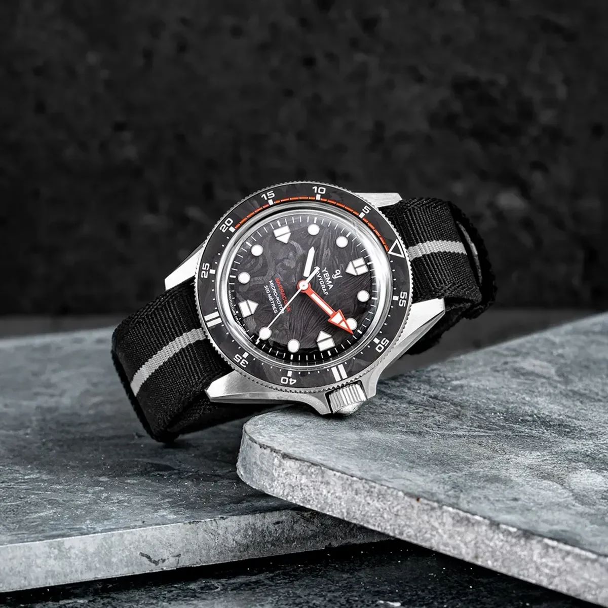 Yema Flygraf Barracuda, textured black dial, black/orange bezel, red second hand, striped NATO strap on slate.