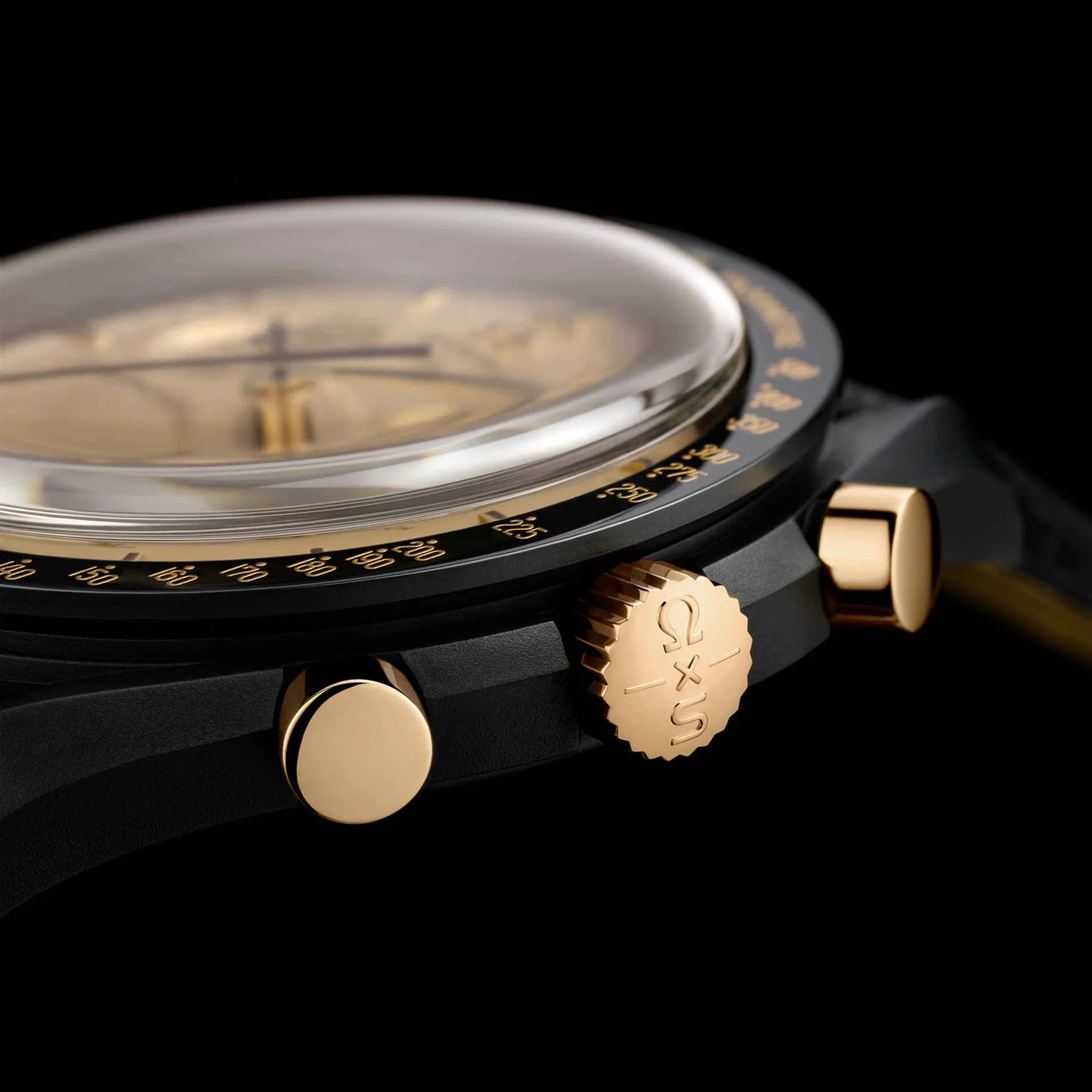 Macro shot of a black watch with gold-toned dial, gold pushers, and a crown engraved with the Omega x Swatch logo.