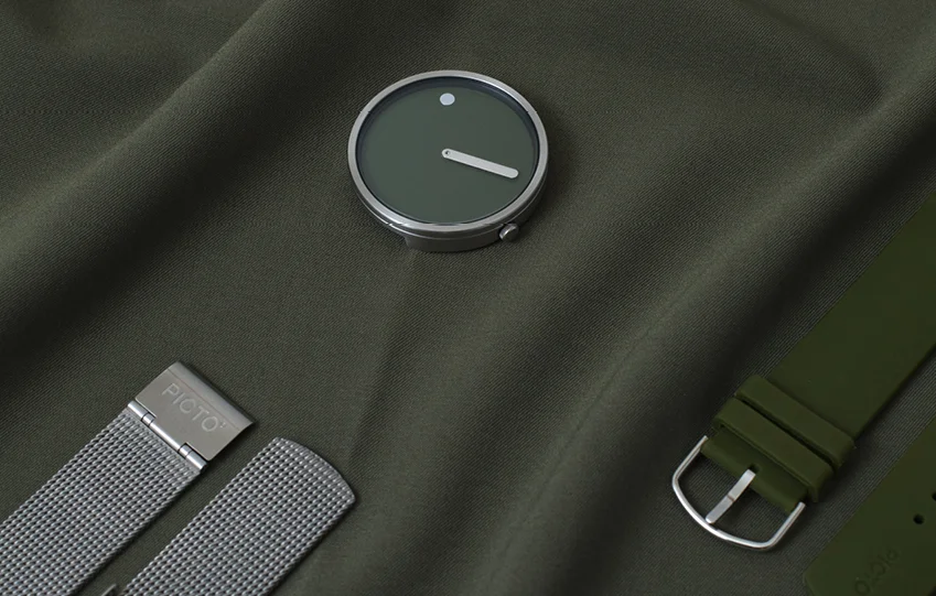 Picto watch with olive green dial, white dot/bar, beside silver mesh and green rubber straps on olive fabric.