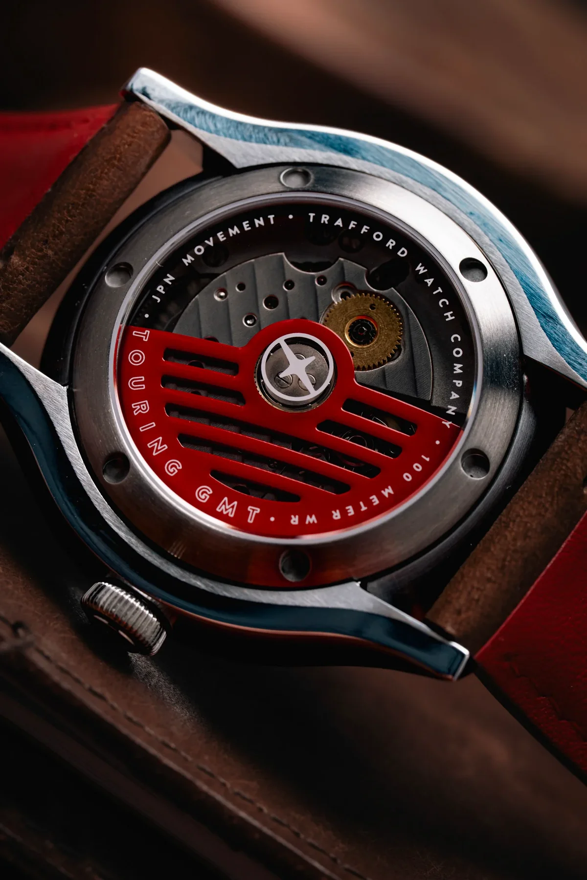 Trafford Touring GMT watch's exhibition case back showing red rotor, movement, crown, and red leather strap.