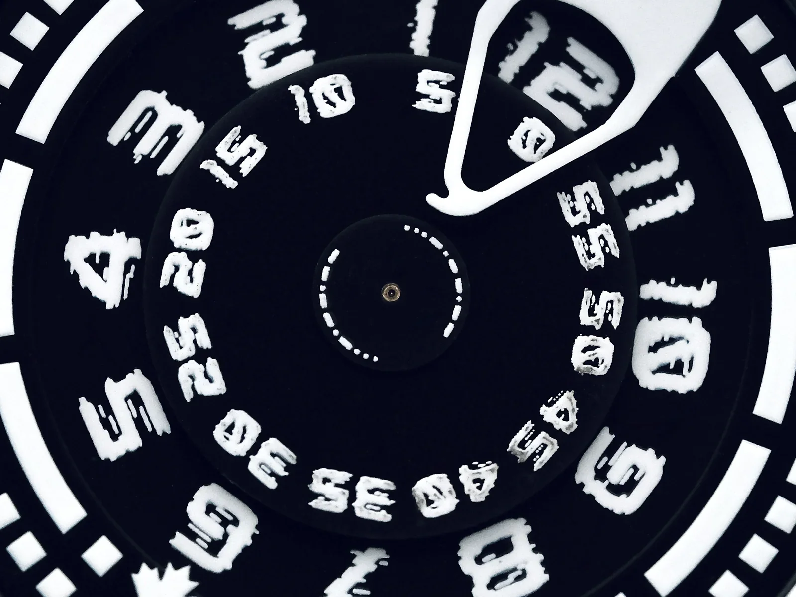 Close-up: black watch dial with distinctive white hour and minute numbers on rotating discs, indicated by a white pointer.