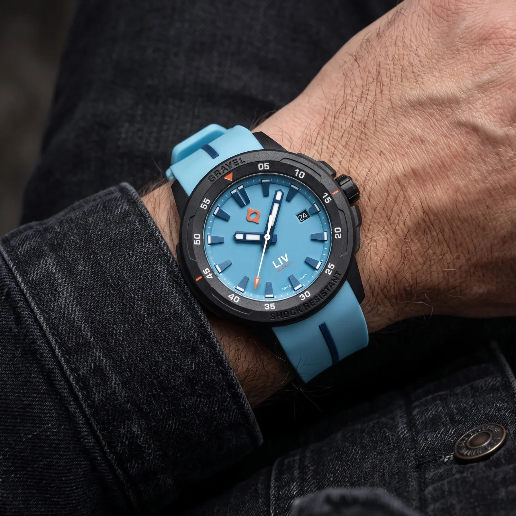 Man's arm wearing a black LIV Gravel watch with light blue dial and matching rubber strap, against a dark denim sleeve.