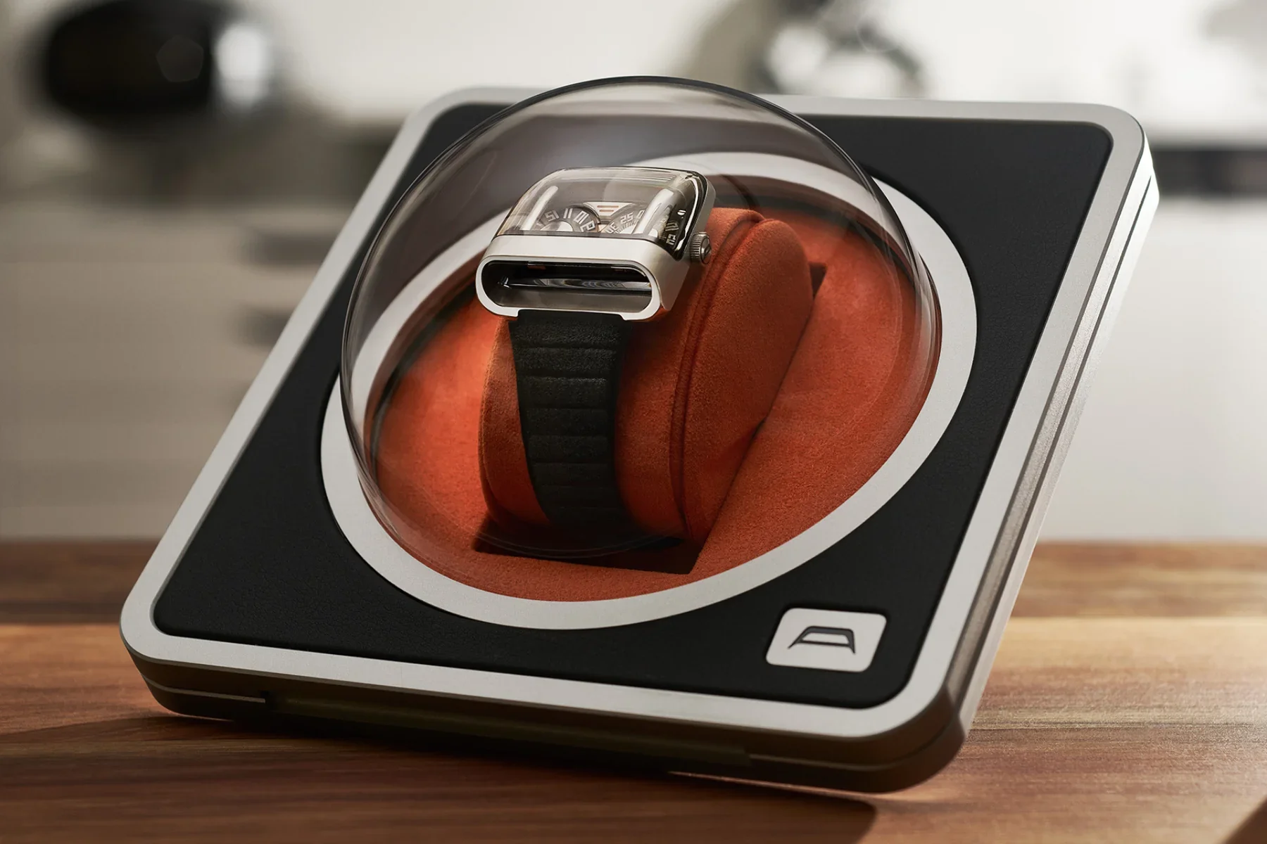Avant-garde watch with black strap in a winder with an orange interior on a wooden table.