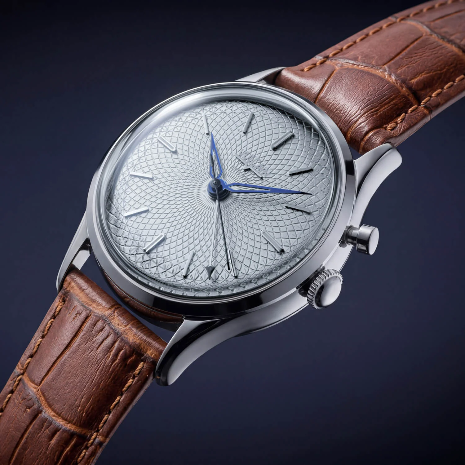 Silver watch with intricate guilloché dial, blued hands, and brown alligator strap against a dark background.