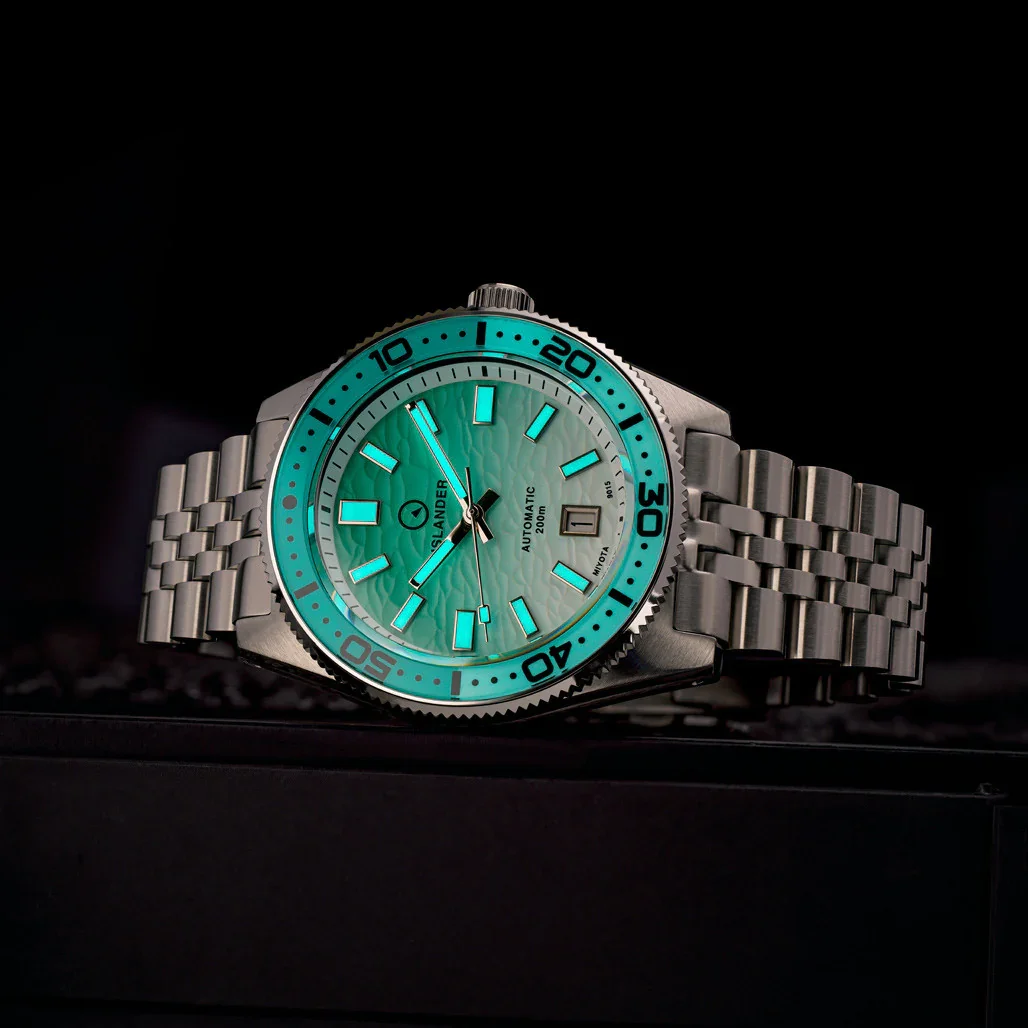 Islander automatic diver watch with steel jubilee bracelet, wave-textured green luminous dial & bezel. Dark setting.