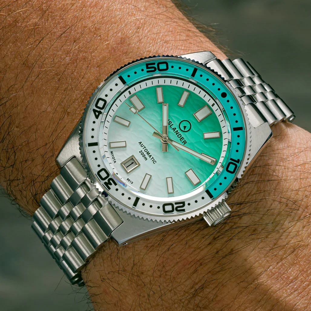 Islander automatic watch with gradient aqua wave-pattern dial, aqua/white bezel, steel jubilee bracelet on arm.