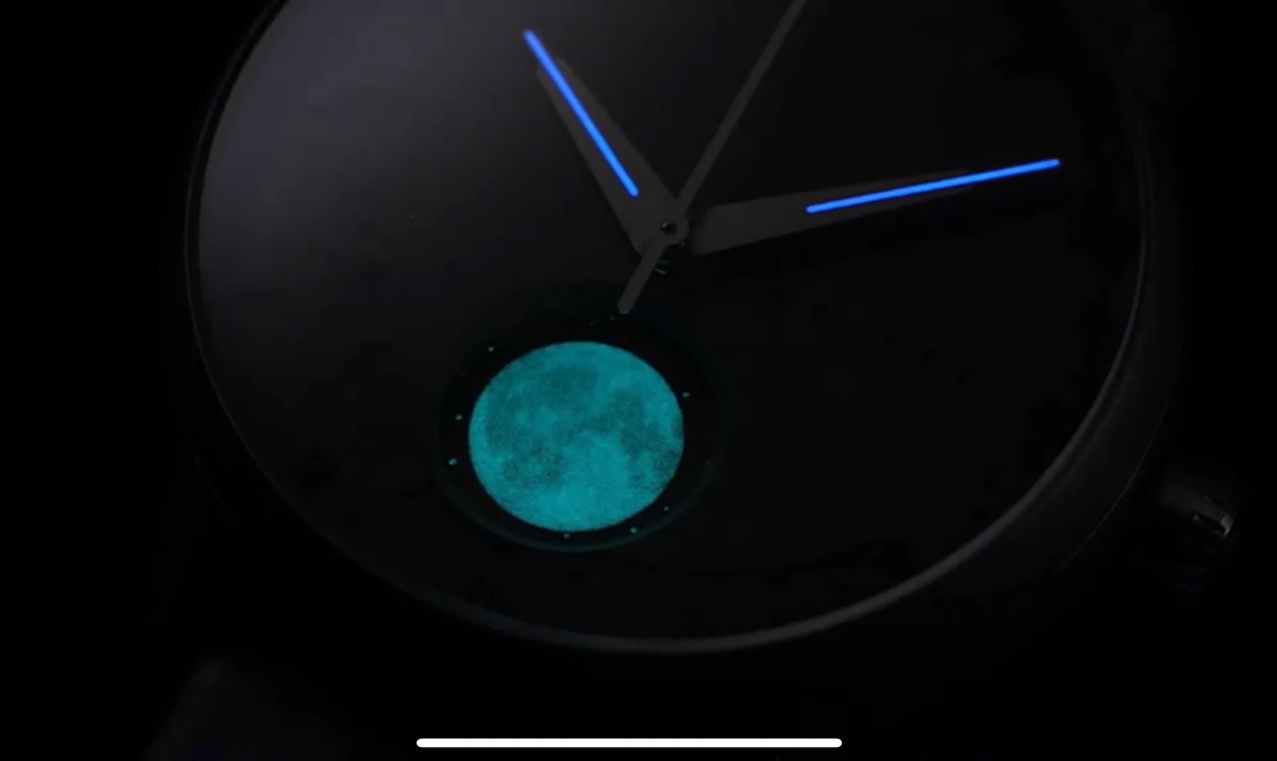Dark luxury watch face with glowing blue hands and a vivid teal moon phase display.