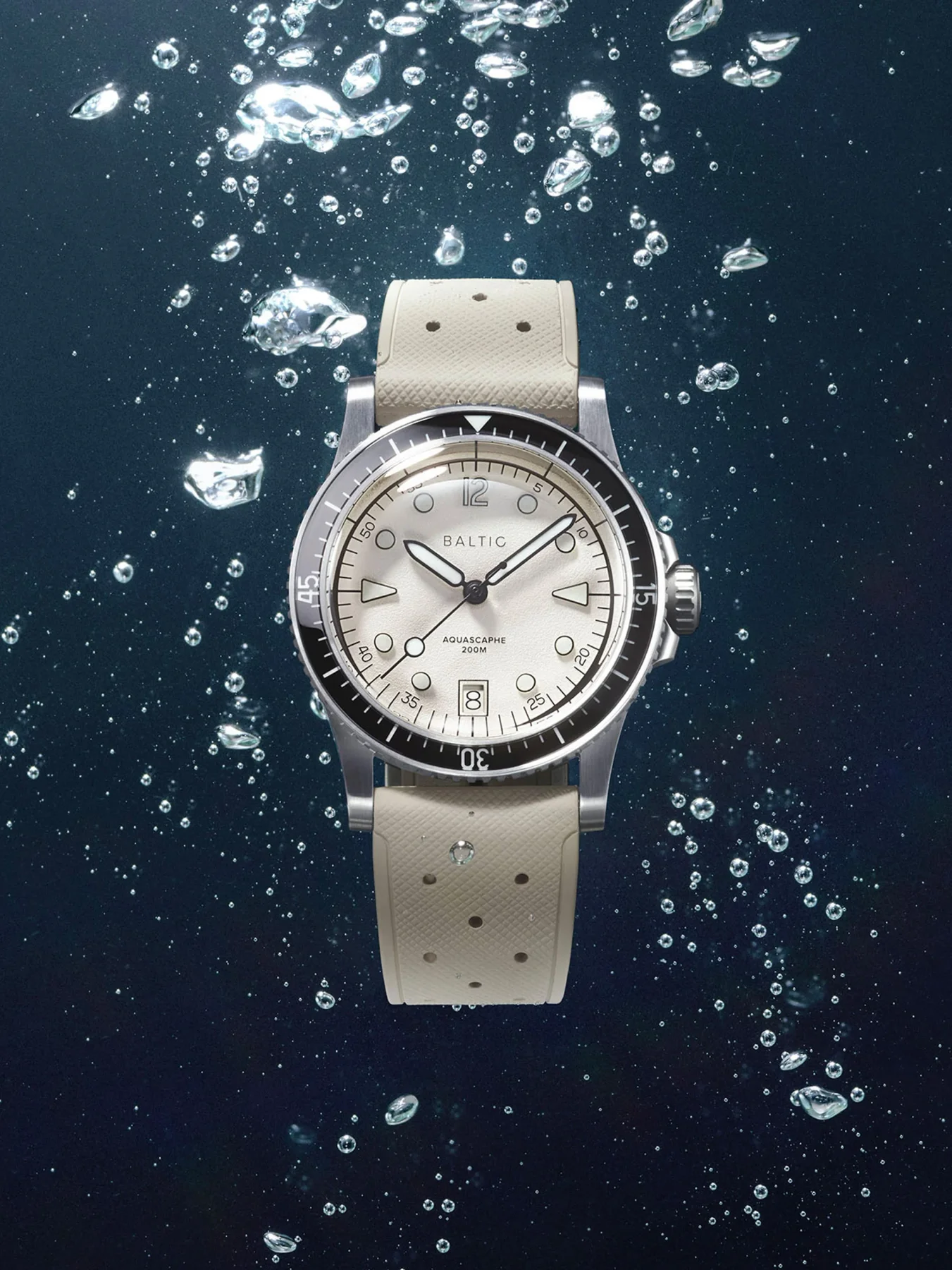 BALTIC Aquascaphe diver watch with cream dial, black bezel, and perforated beige strap floating in dark blue water with bubbles.