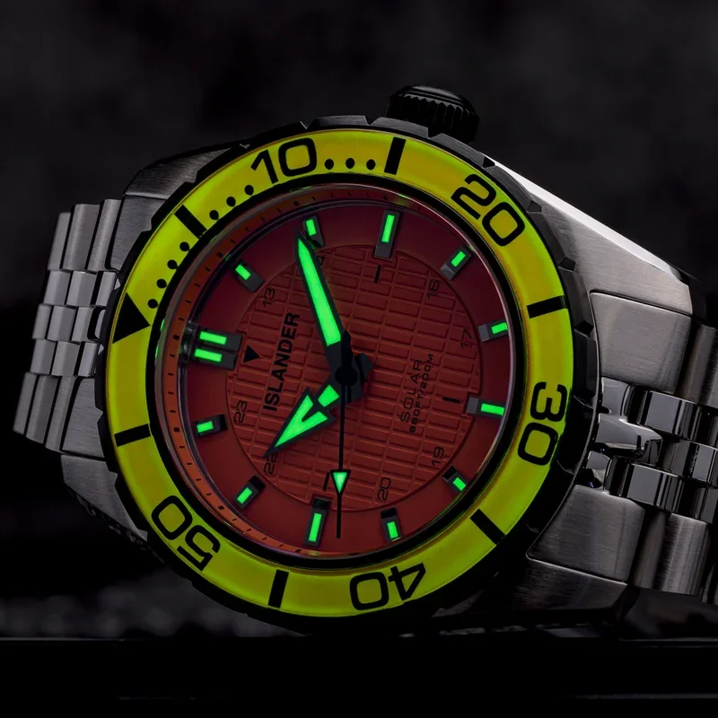 Islander solar diver watch with red textured dial, bright yellow bezel, glowing green hands/markers, & steel bracelet.