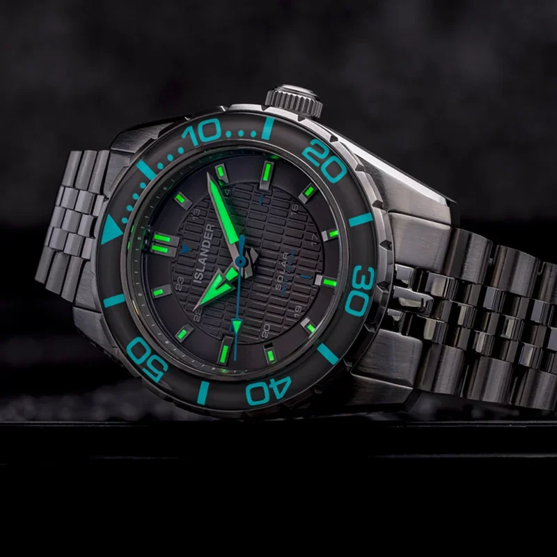 Stainless steel Islander Solar watch with black textured dial, glowing green hands/markers, and black bezel with teal numbers.