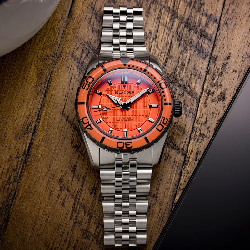 Islander Solar watch, textured orange dial & dive bezel, SS jubilee bracelet on wooden table with phone edge.