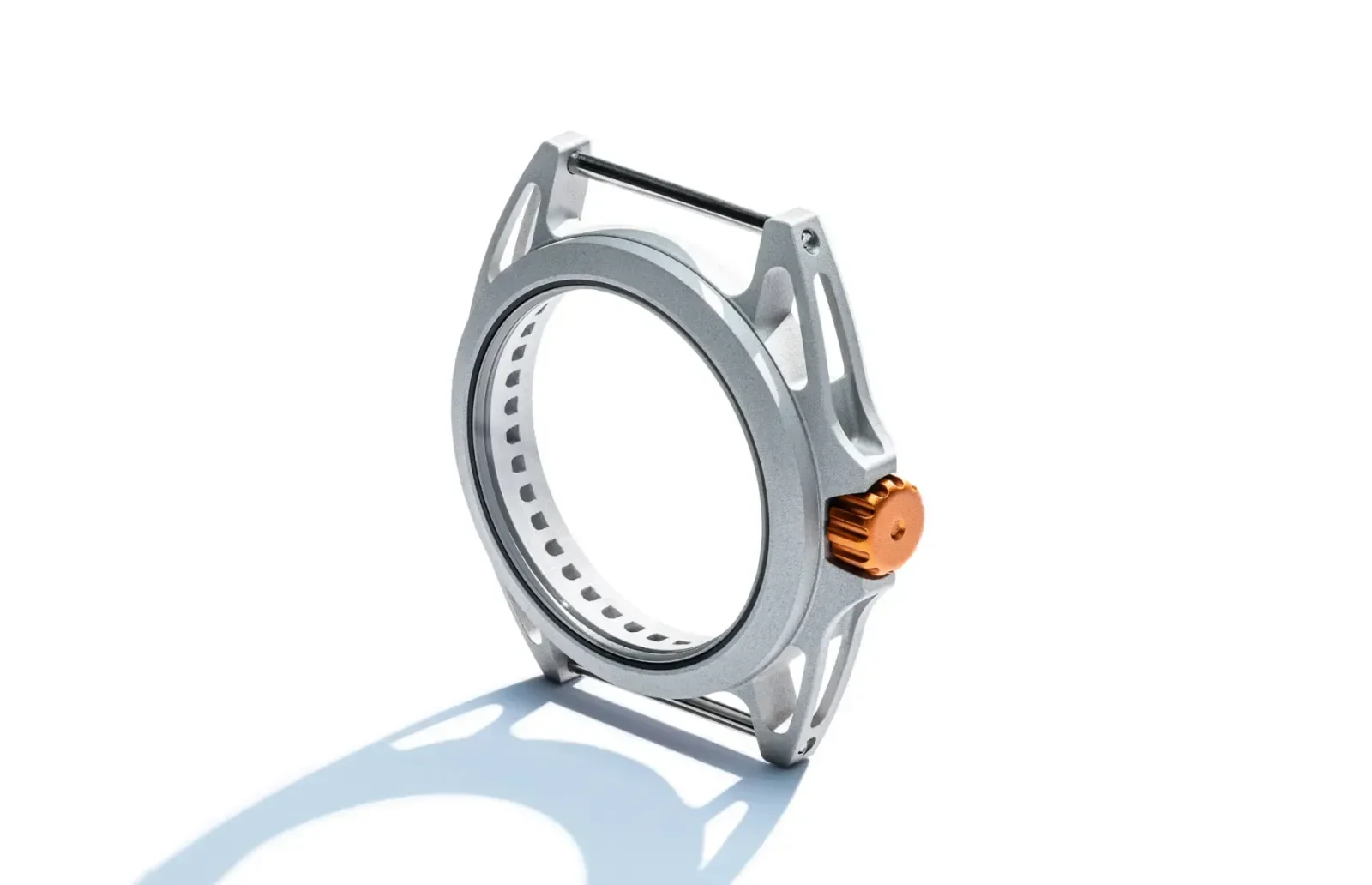 Empty, skeletonized silver watch case with orange crown, on white background with shadow.