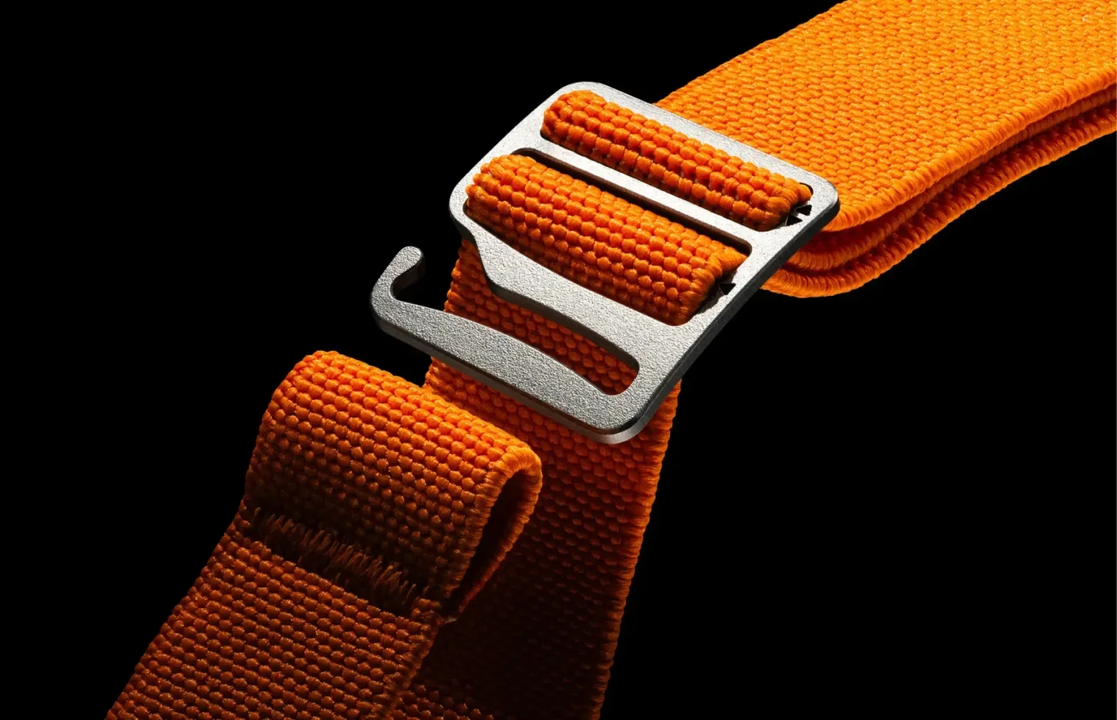 Close-up of orange woven watch strap with silver-colored hook buckle on black.
