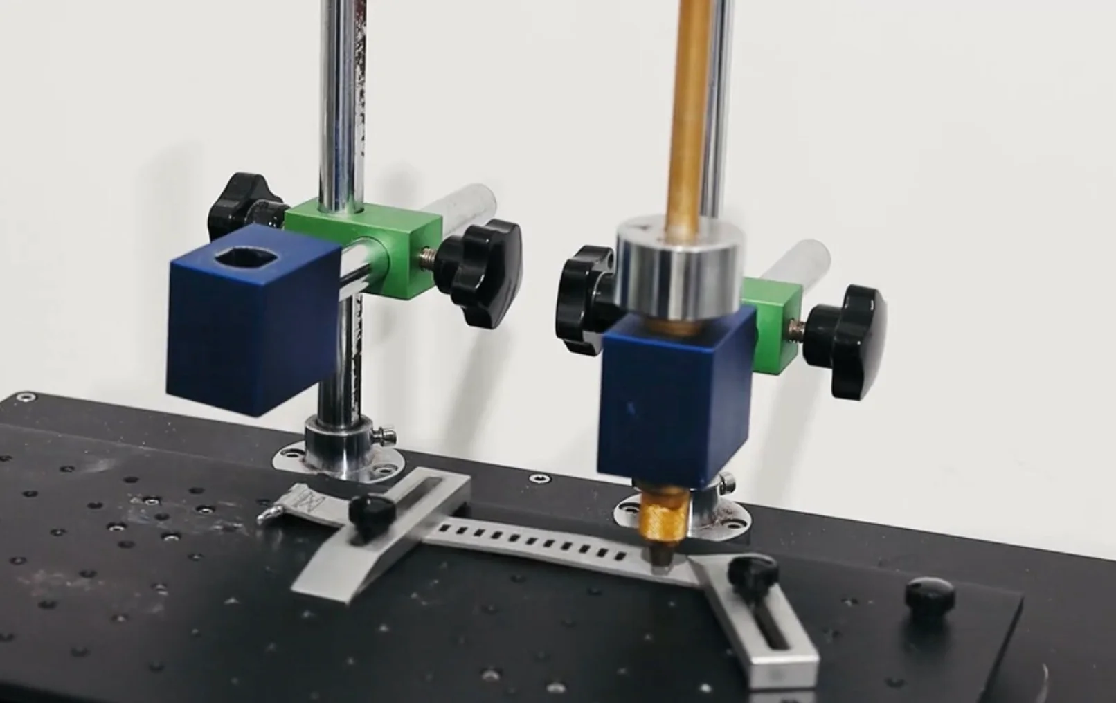 Durability testing machine with a gold-tipped tool pressing a metal watch bracelet link on a black base.