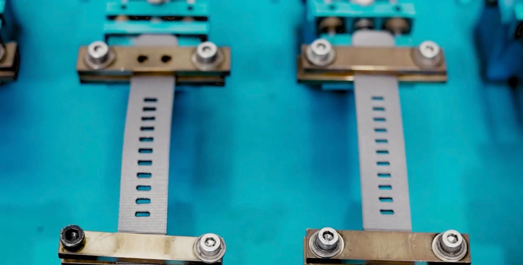 Two light gray perforated watch straps fastened by metal clamps against a vibrant blue background.