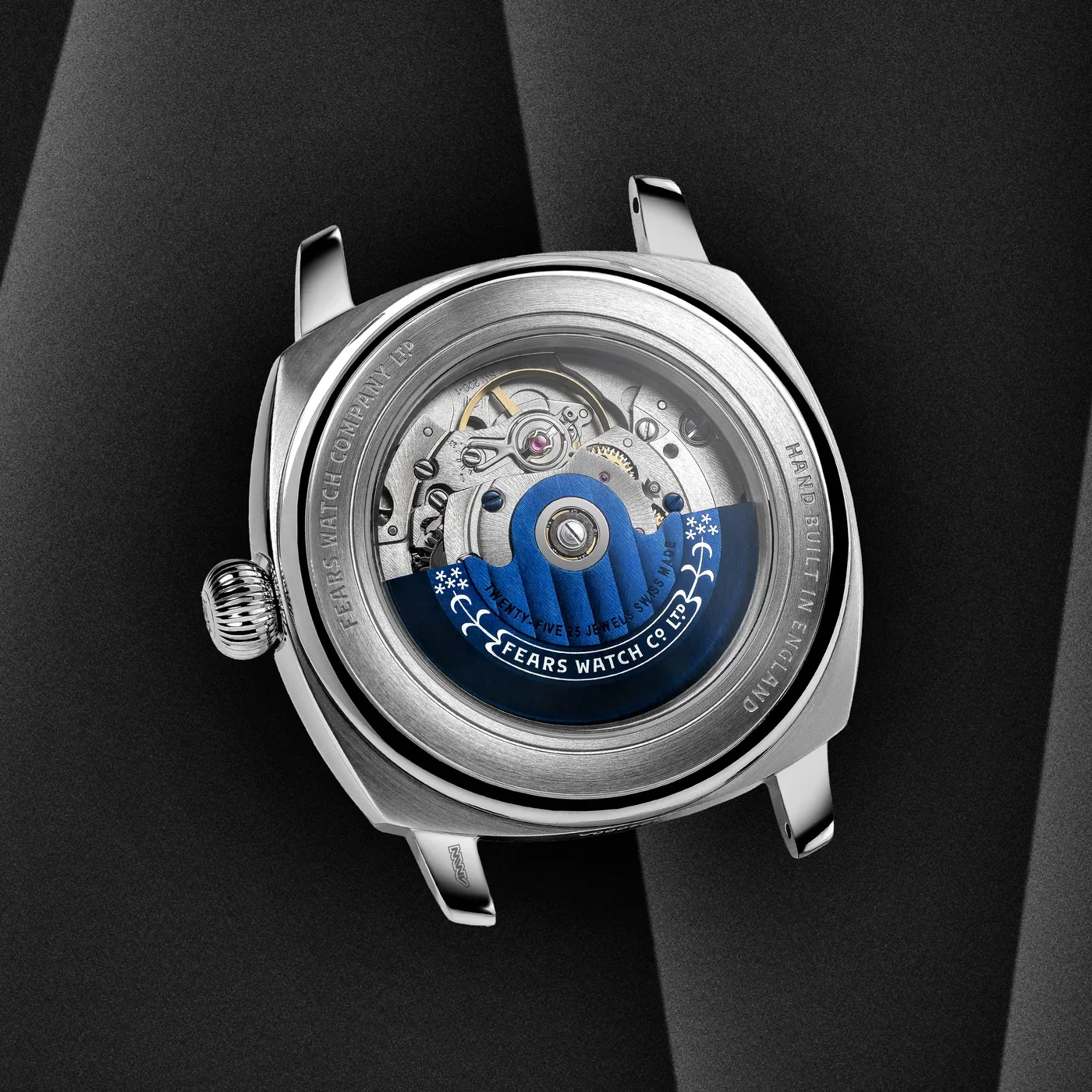 Back of a silver Fears watch. Exhibition caseback shows blue rotor and mechanical movement. "Hand Built in England" text.