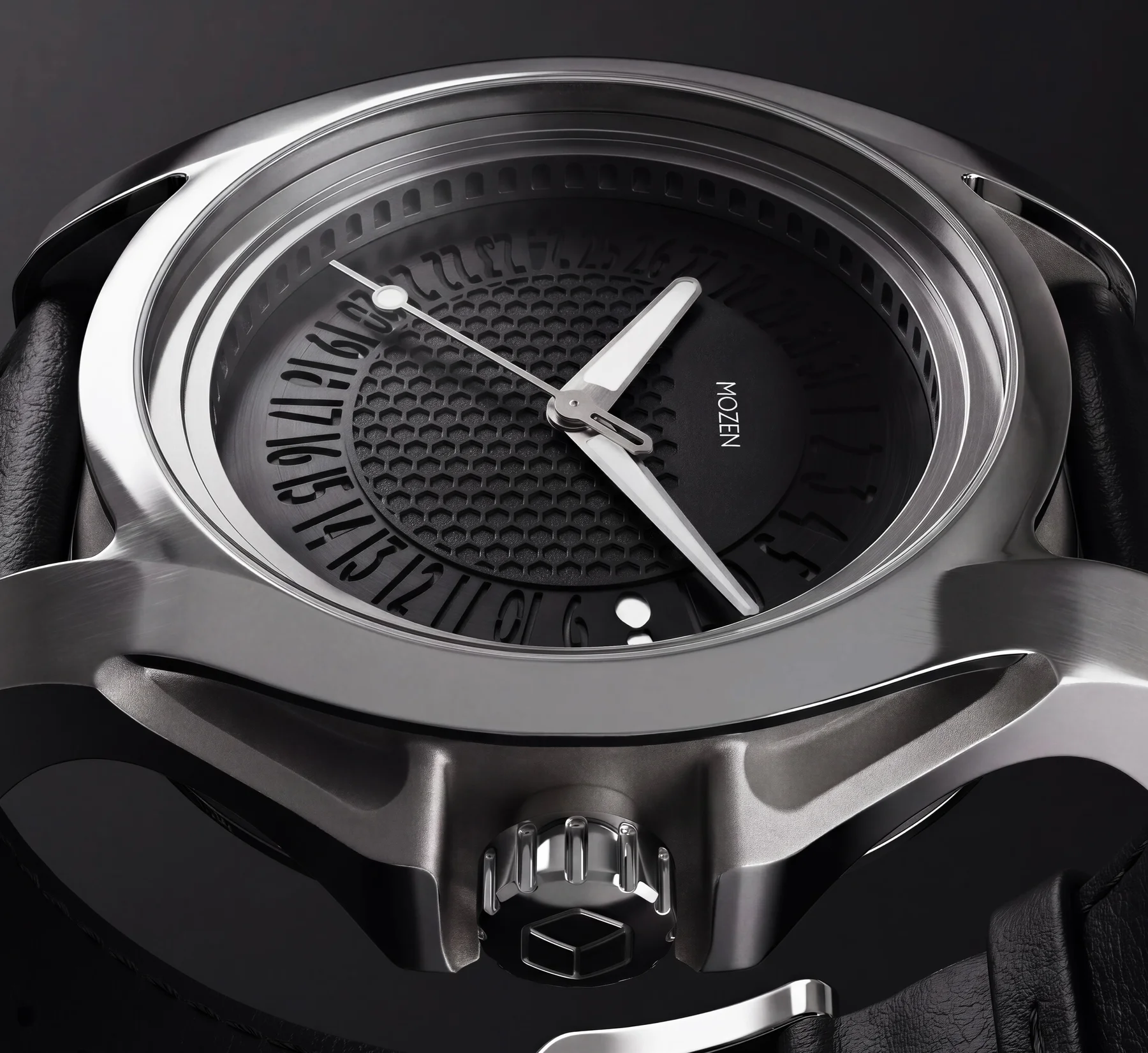Close-up of a polished steel Mozen watch. Black honeycomb dial, white hands, rotating date wheel, leather strap.