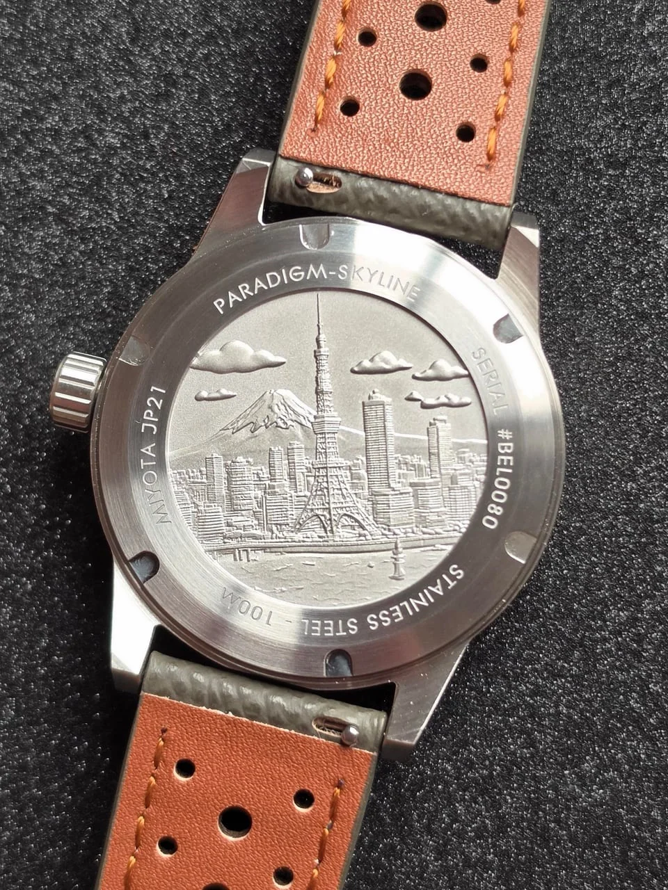 Stainless steel watch back engraved with Tokyo cityscape, Mt. Fuji, and Tokyo Tower. Tan perforated leather strap.