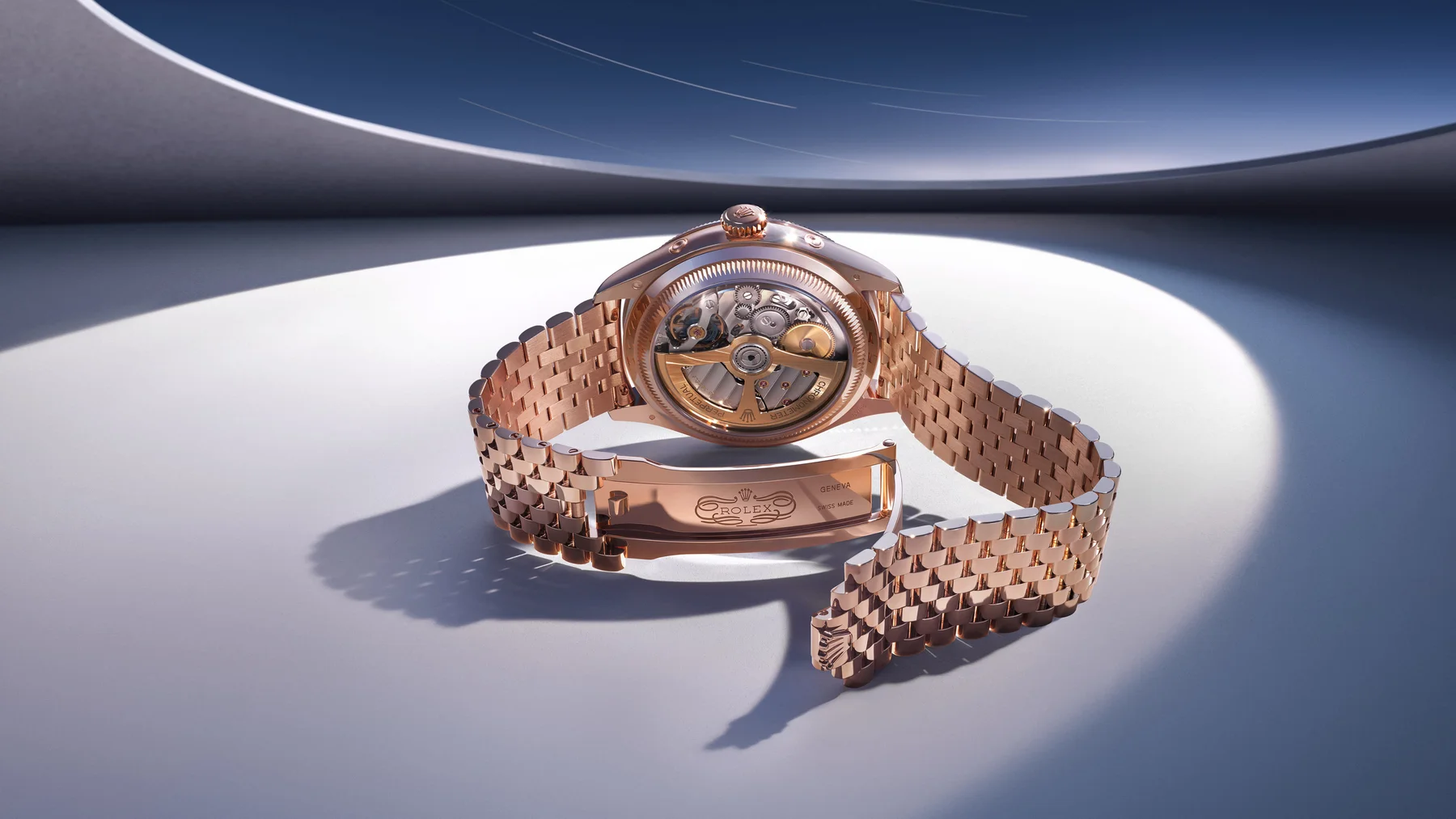 Rose gold Rolex watch with exhibition case back, open bracelet, in a minimalist studio setting.