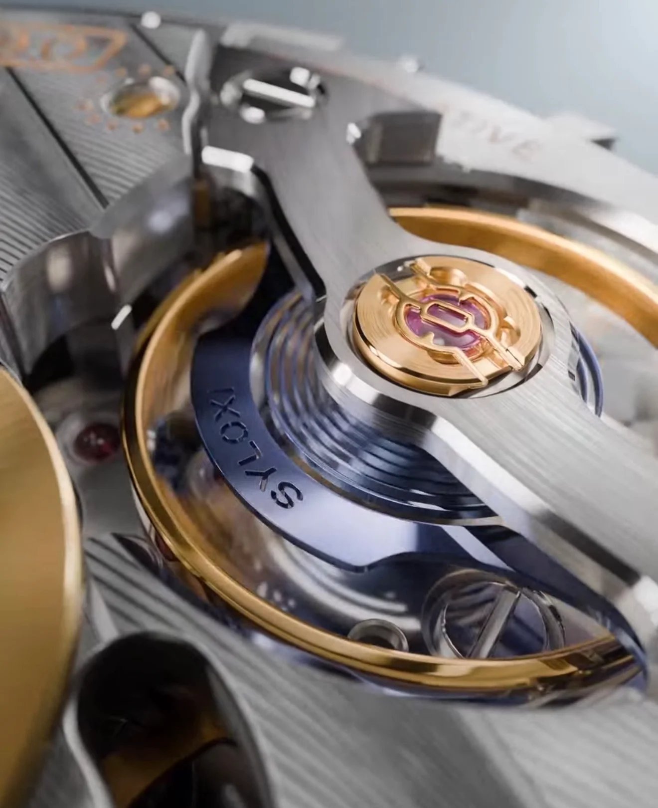 Intricate luxury watch movement showing brushed silver, polished gold components, a balance wheel with a ruby, and 
