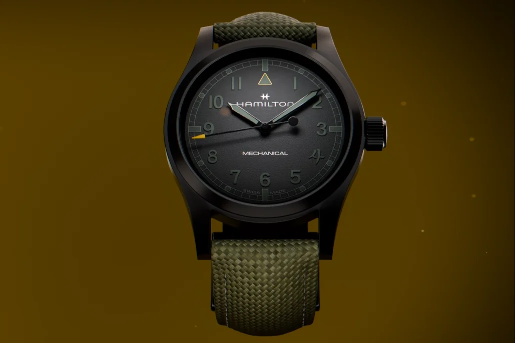 Hamilton Mechanical watch: black case, dark green dial, green hands with yellow second hand, olive textile strap, gold background.