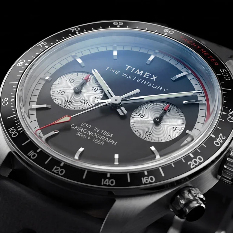 Close-up of a Timex Waterbury Heritage Chronograph. Dark gray dial, silver subdials, red accents, steel case & tachymeter bezel.
