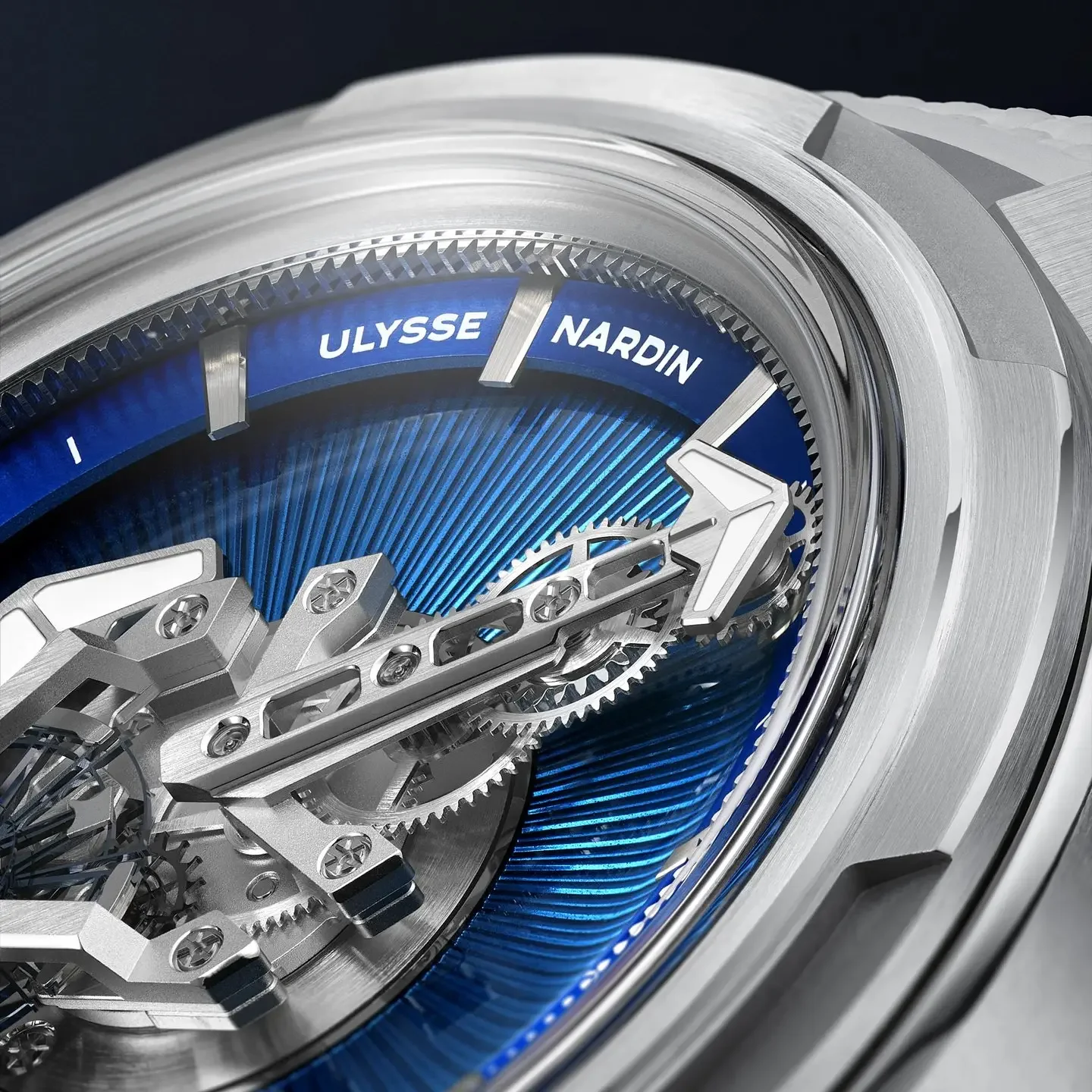 Silver Ulysse Nardin watch with vibrant blue textured dial, visible gears, and arrow-shaped hands.