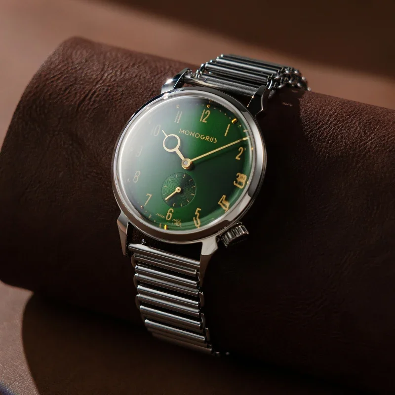 MONOGRIIS watch with a green dial, gold numerals, and silver case on a metal bracelet, on brown leather.