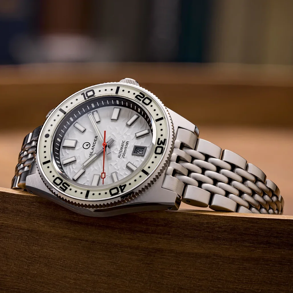 Silver Islander dive watch with hammered white dial, red second hand, and metal "beads of rice" bracelet on wood.