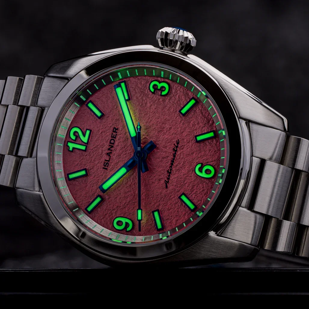 Islander watch: textured red parchment dial, glowing green bar markers & 3, 6, 9, 12 numerals, blued hands, steel bracelet.