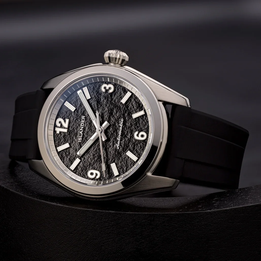 Islander automatic watch with silver case, textured black dial resembling parchment, white numerals, and black rubber strap.