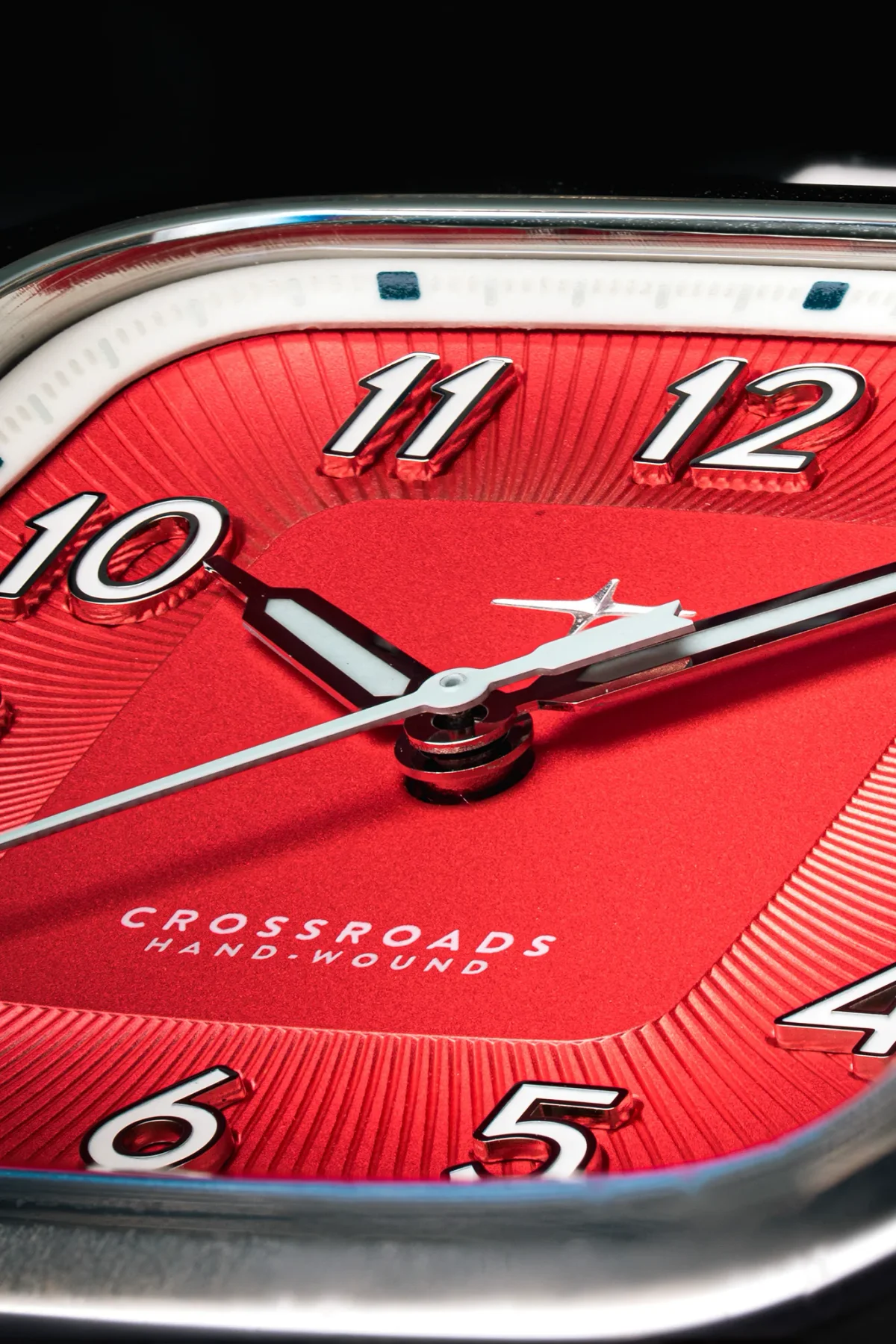 Macro shot of a Crossroads Hand-Wound watch: red dial with sunburst texture, white numerals, silver hands.